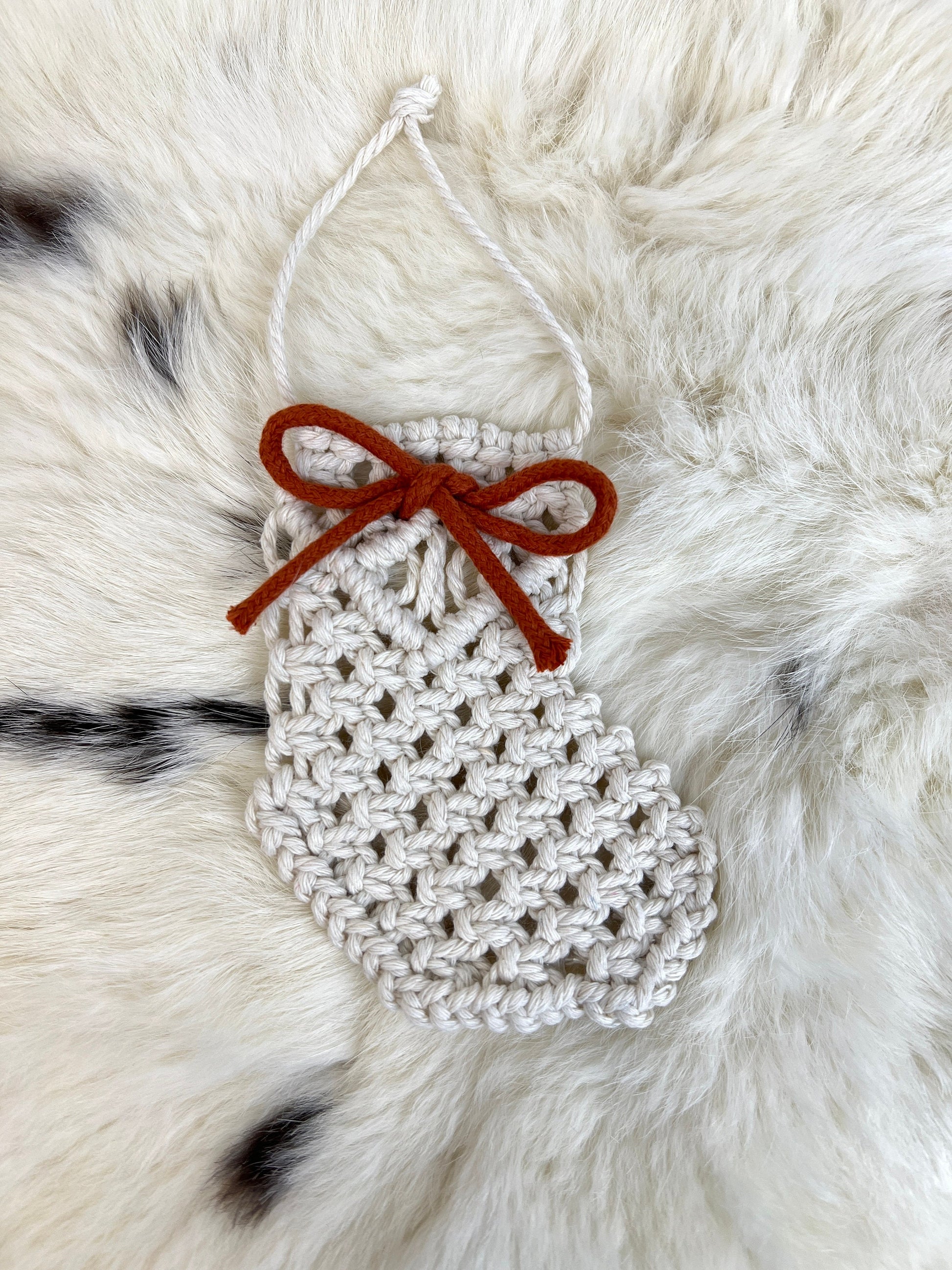 Macrame white Christmas ornament with a red bow on a fur background