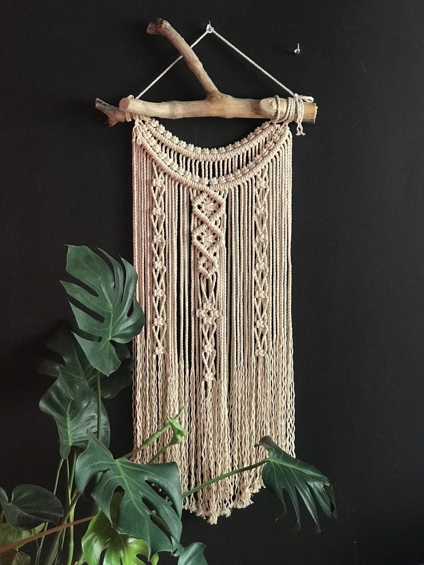 Macrame wall hanging on a branch against a black background