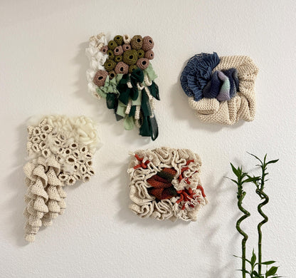 Four crocheted wall art pieces on a white background with a plant on the right.