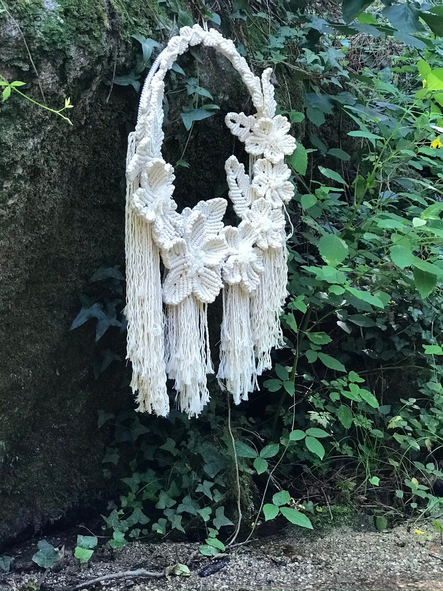 Decorative white macrame wall hanging with floral designs against a natural background.