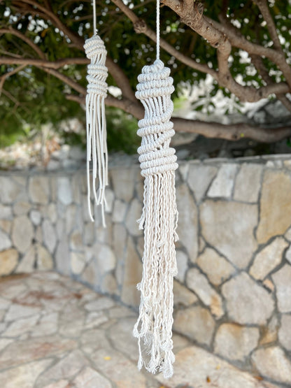Two macrame jellyfish hangings hanging from a tree with a stone wall and greenery in the background.