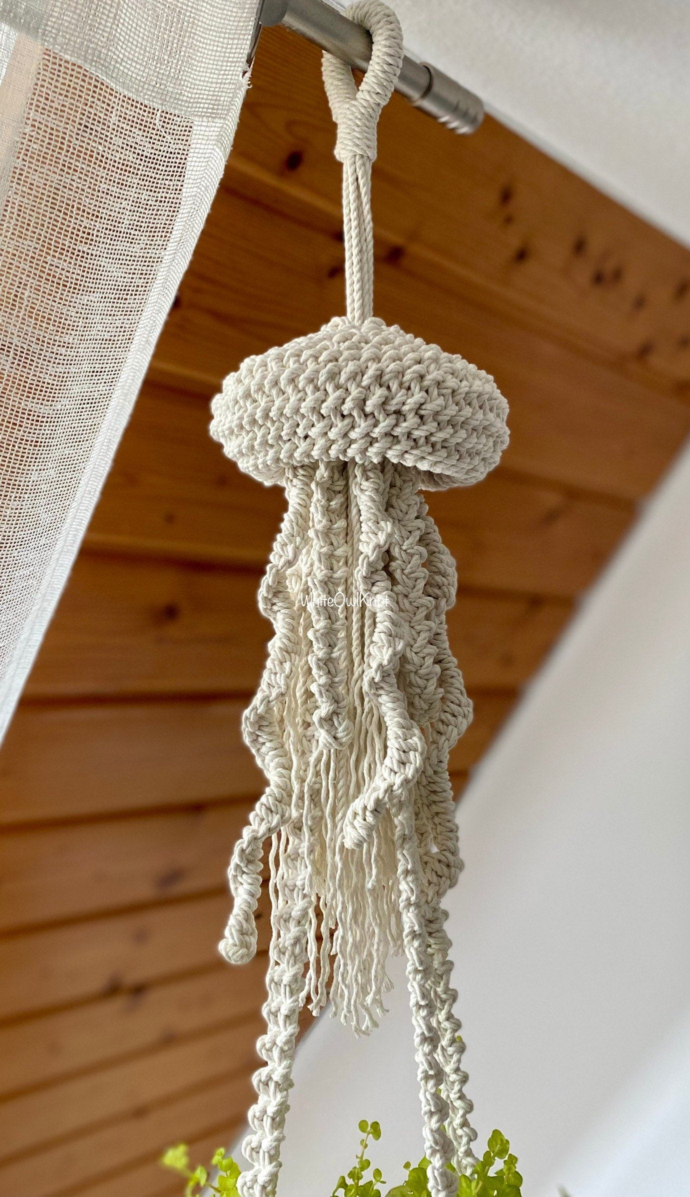 Knitted plant hanger hanging from a wooden ceiling