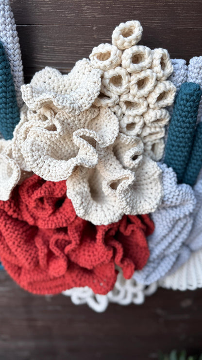 Crocheted and macrame coral reef details in various colors on the wooden surface