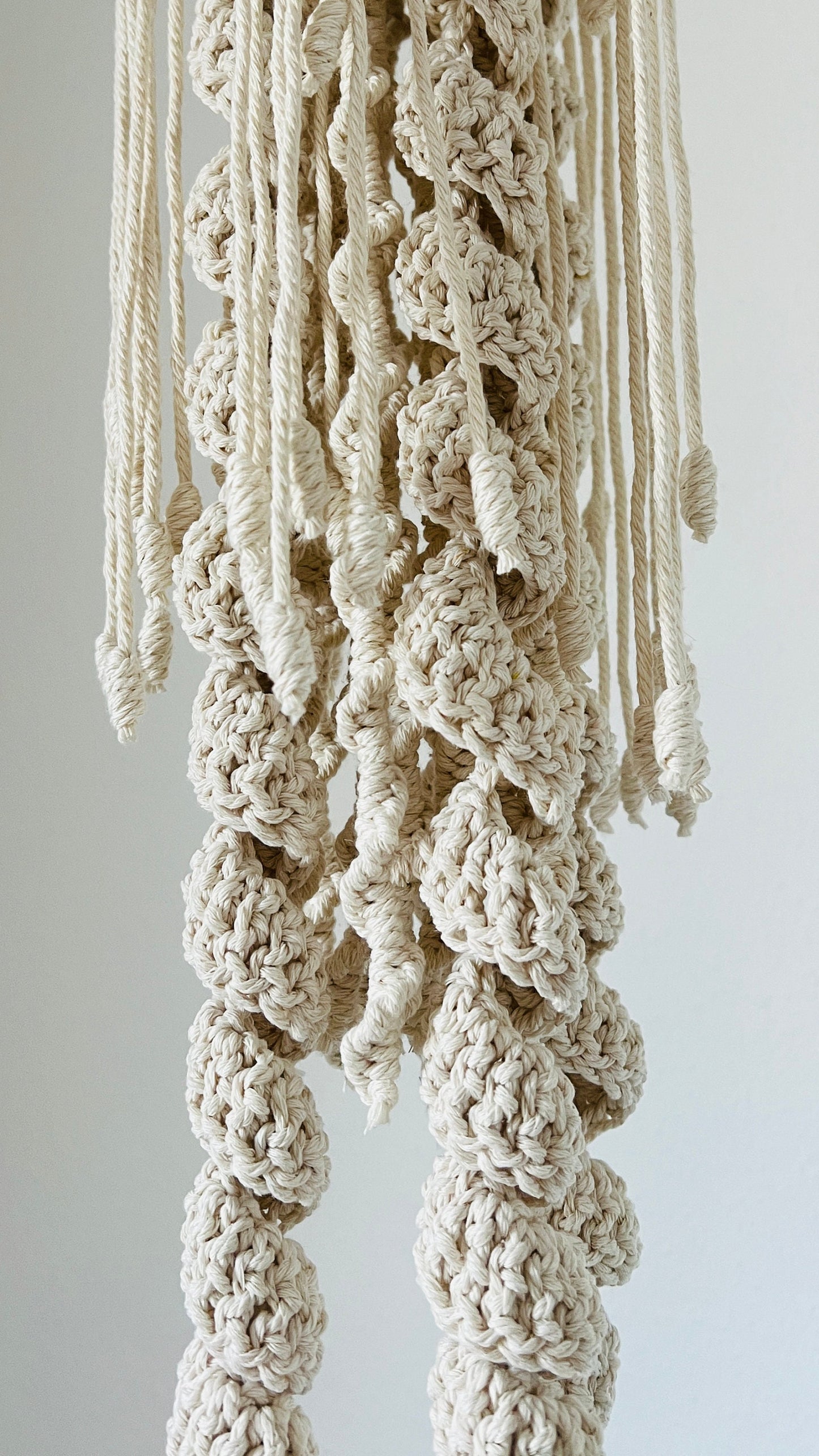 Close-up of a textured, beige woven jellyfish tentacles against a plain background
