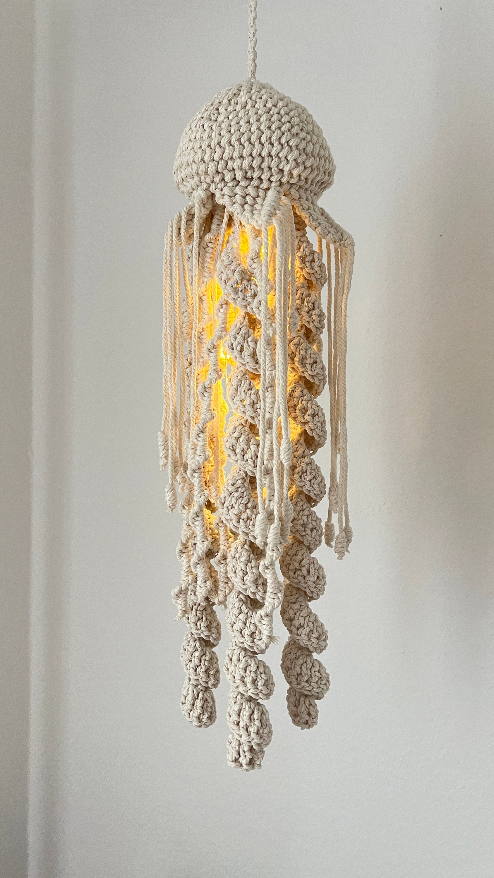 Macrame jellyfish-shaped lamp with a warm glow on a plain background
