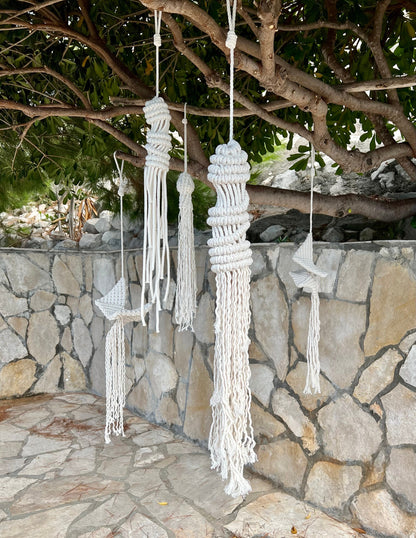 Macrame wall hangings hanging from a tree against a stone wall.