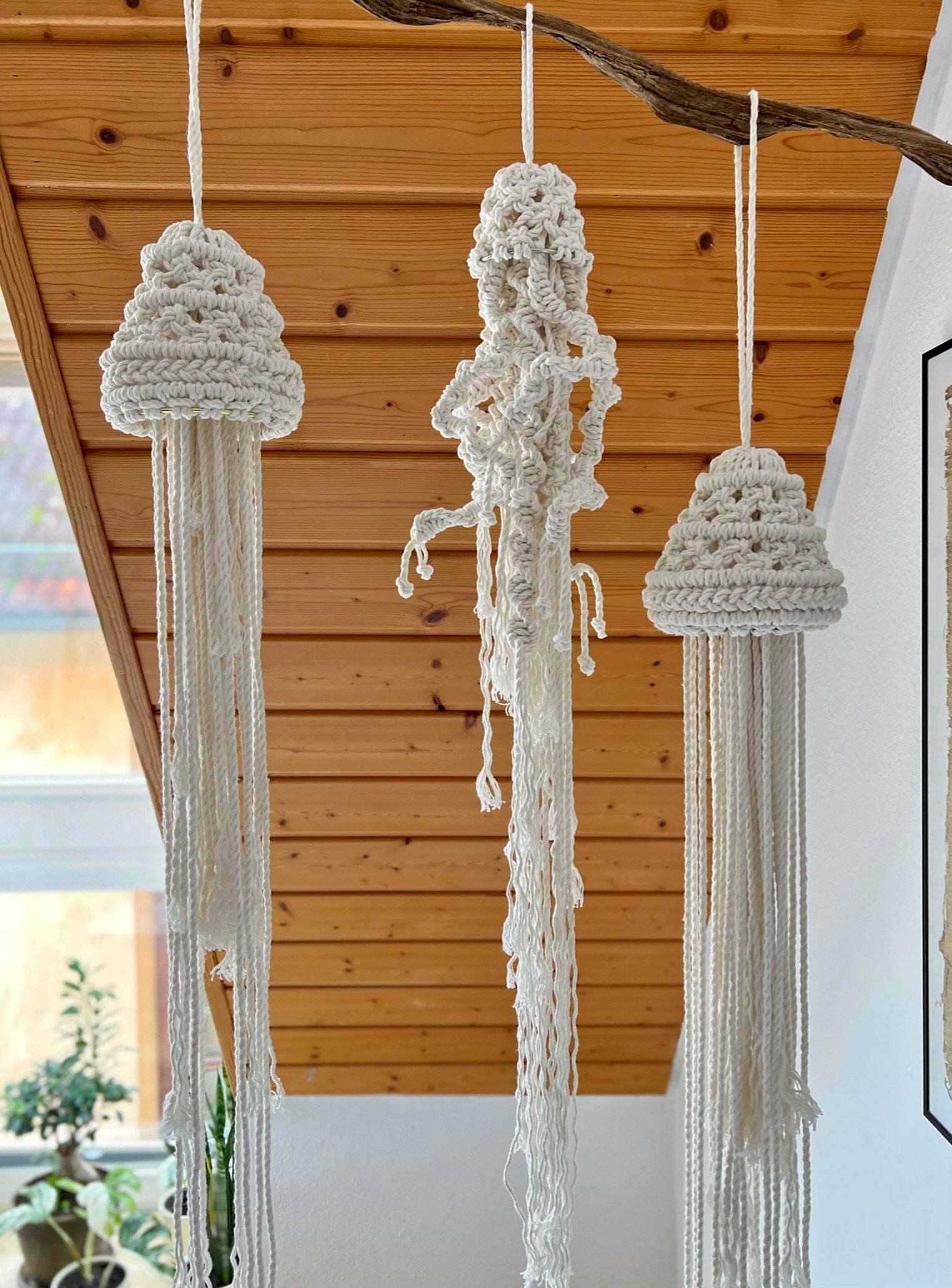 Three macrame hanging jellyfish of different sizes hanging from a ceiling.