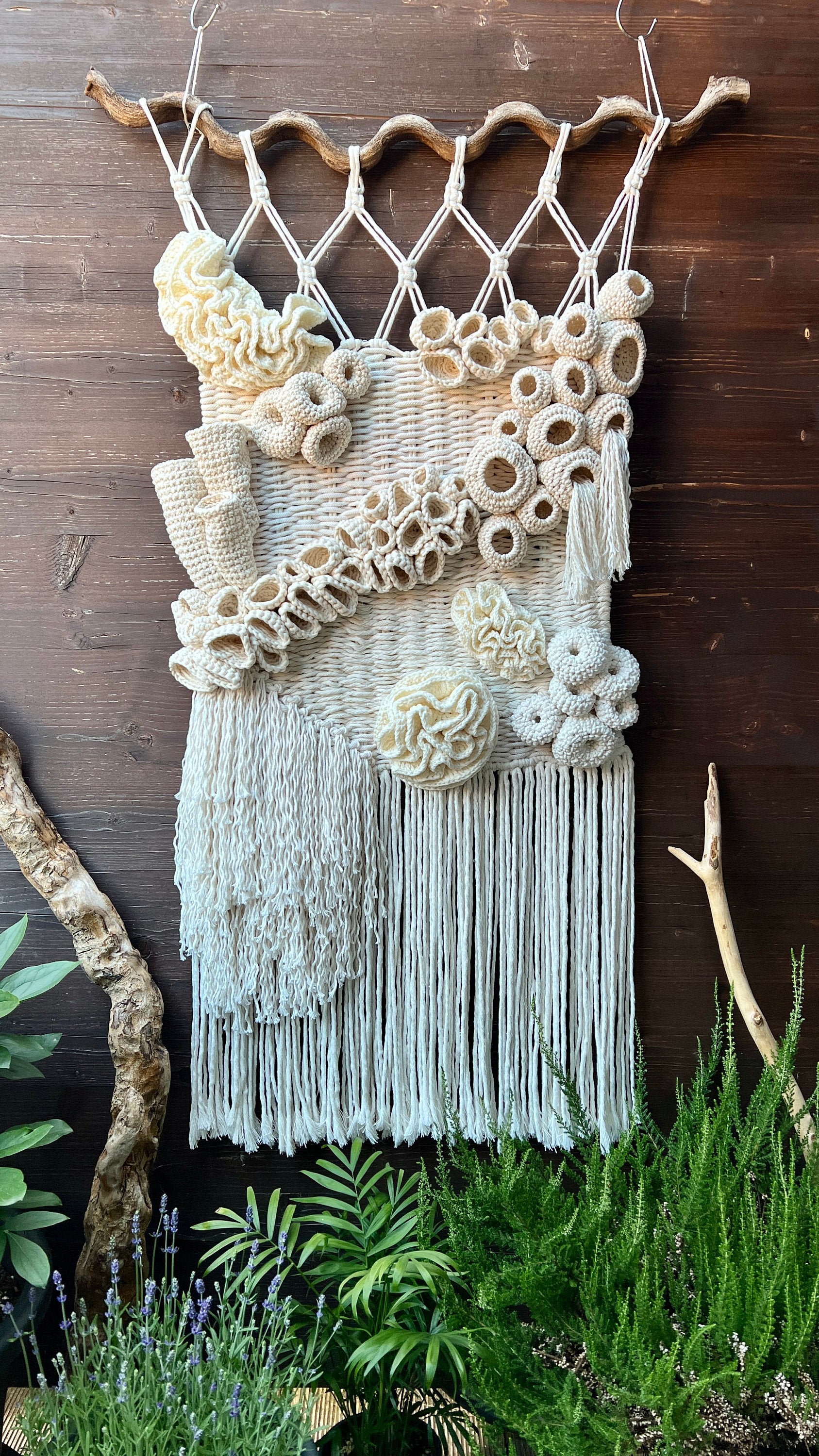 Textile art piece with coral reef detail and fringes on a wooden wall