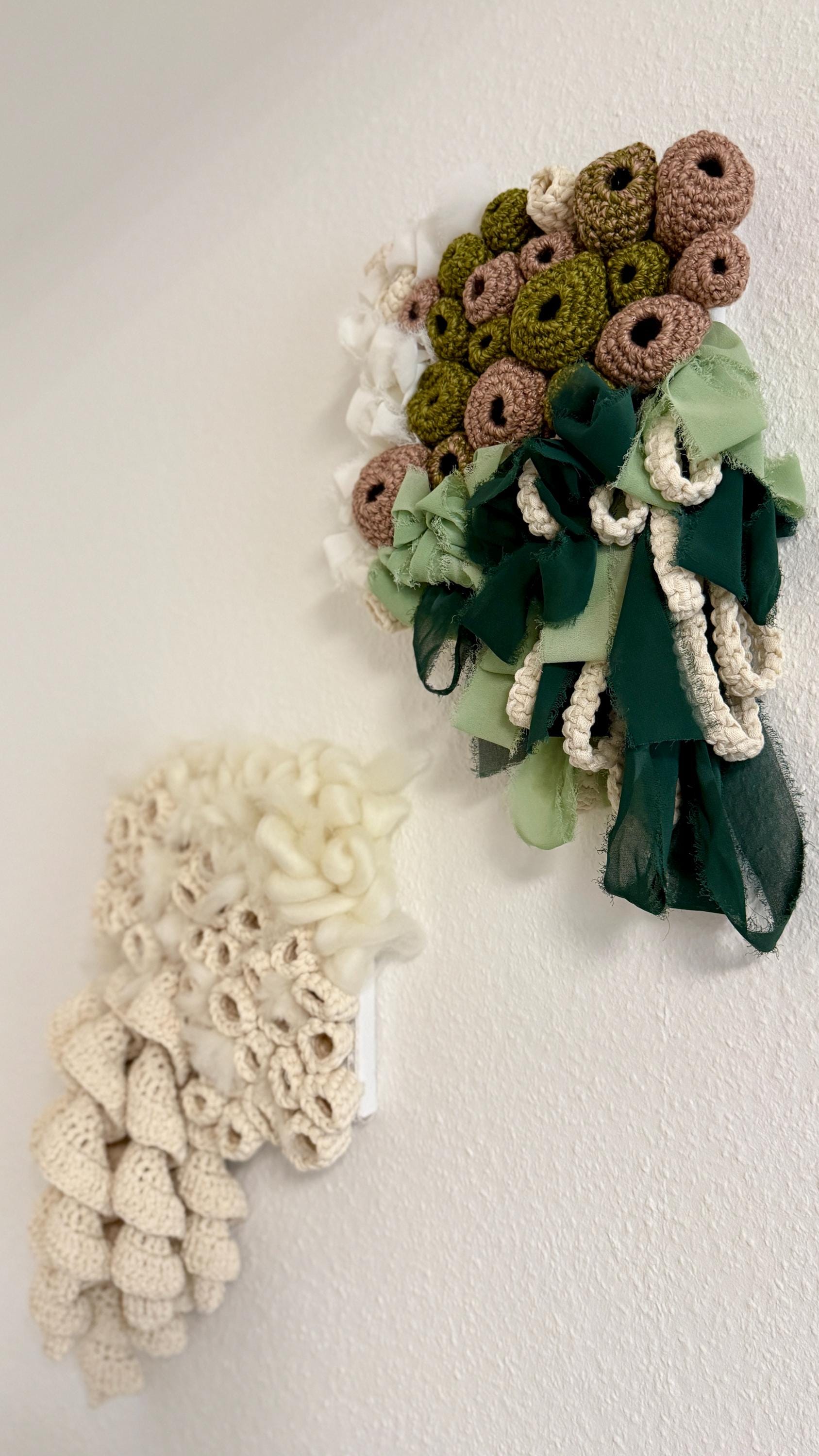 Crocheted wall art piece with green and white colors on a plain background