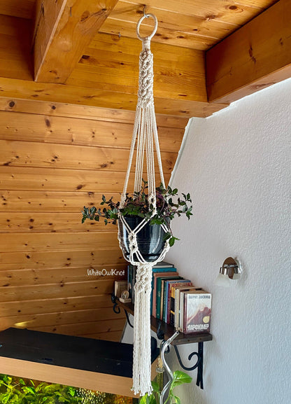 Macrame plant hanger with a plant against a wooden wall and white wall.