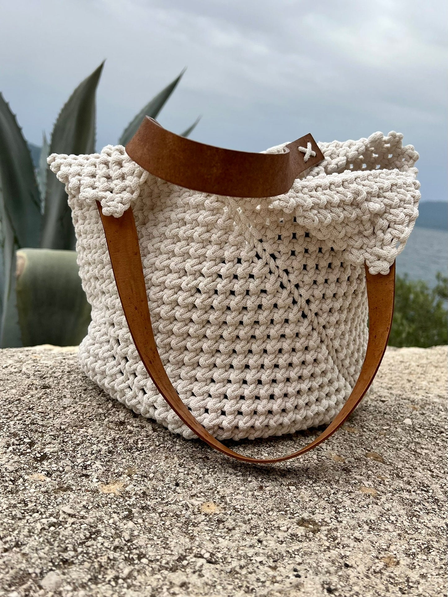 Macrame bag with a brown strap on a stone surface with a scenic background