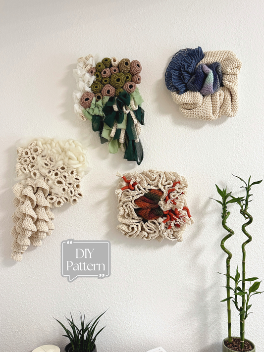 Decorative wall art pieces made from crochet or knit materials on a white wall with a plant in the corner.