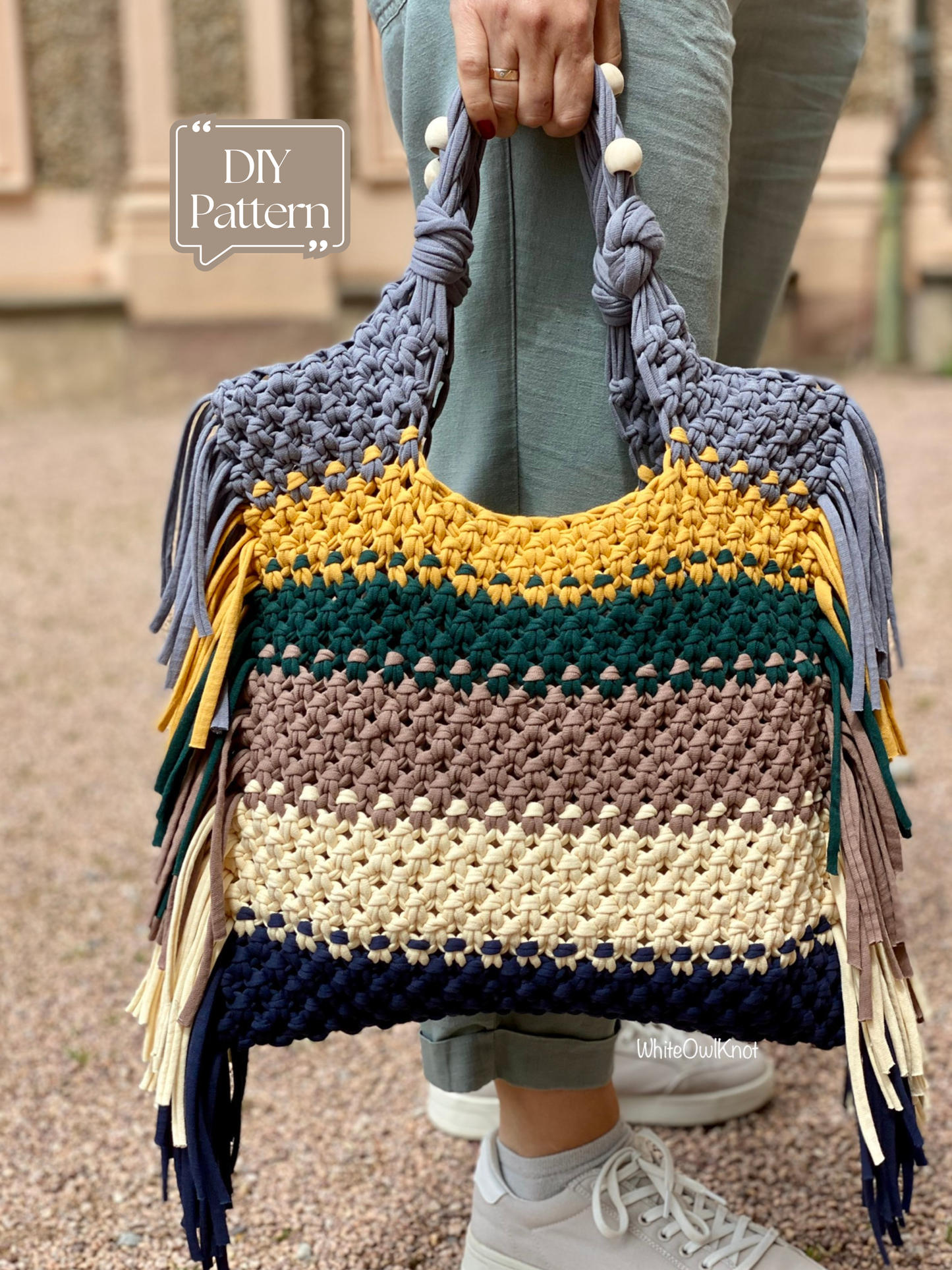 Colorful macrame handbag with fringe held by a person outdoors.
