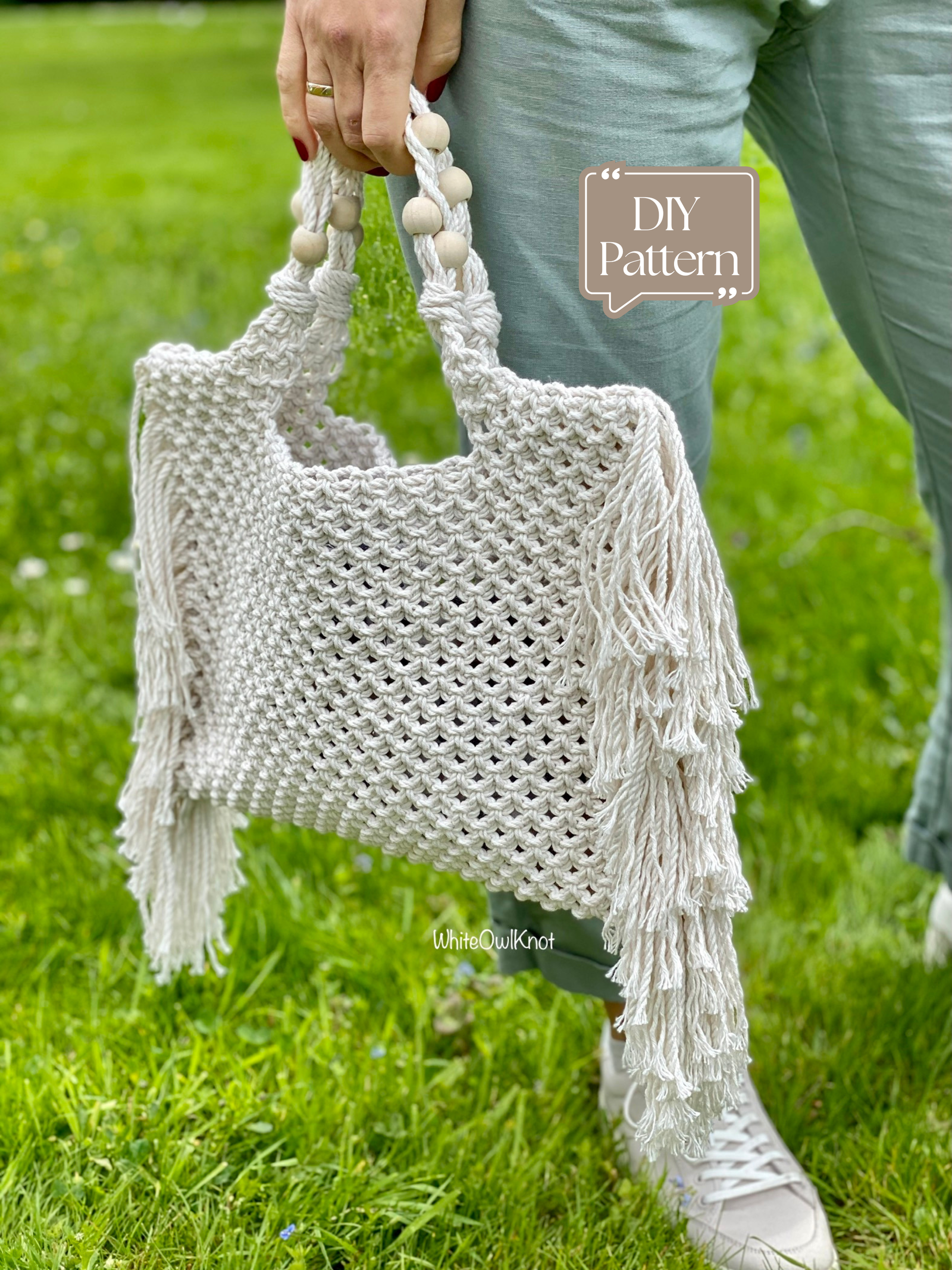 Person holding a white macrame bag with fringe on a grassy background
