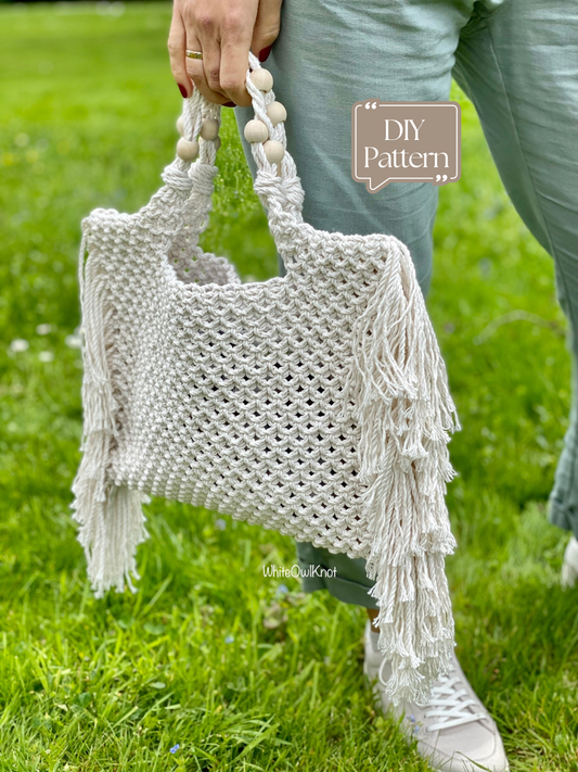 Person holding a white macrame bag with fringe on a grassy background