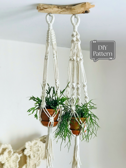 Set of two white macramé plant hangers holding small potted plants, hanging indoors from a wooden branch; DIY macramé PDF pattern.