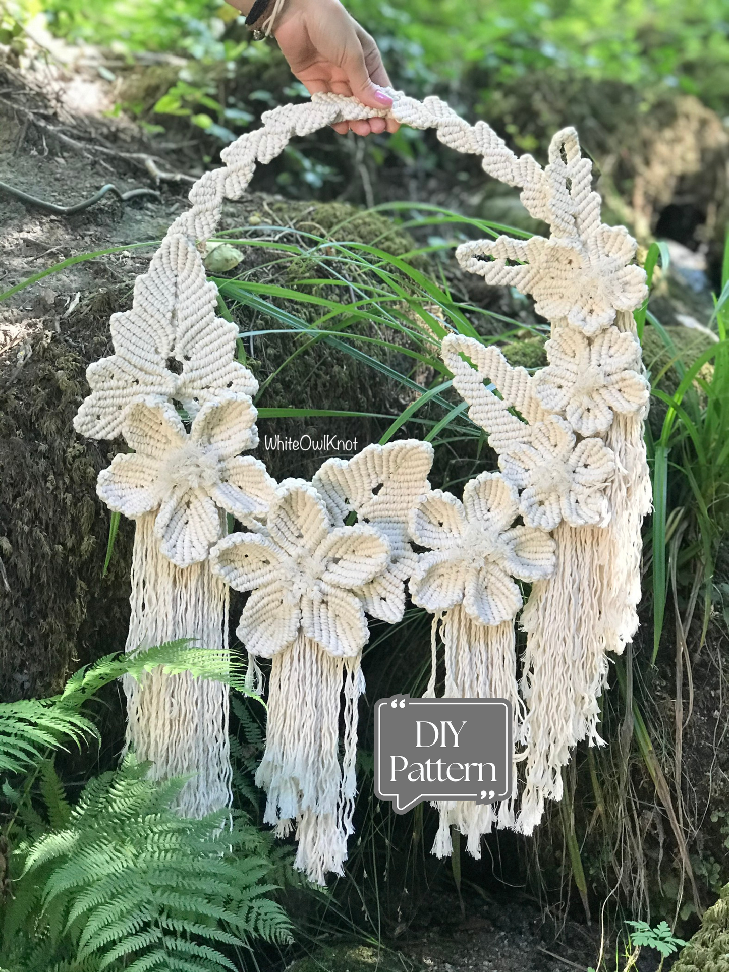 Macrame wall hanging with floral designs held by a hand against a natural background.