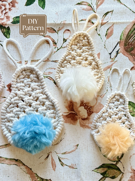 Macramé Easter bunny ornament with woven rope body, long bunny ears, and a soft blue pom-pom tail, shown on a floral fabric background, DIY macramé pattern.