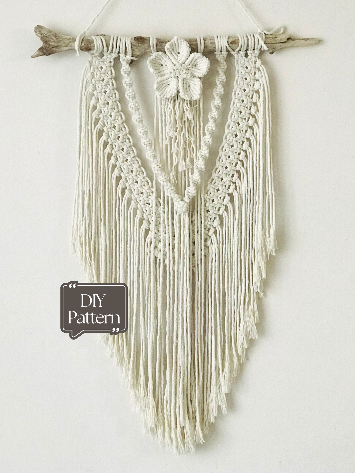 Macrame wall hanging on a white wall with a plant in the foreground