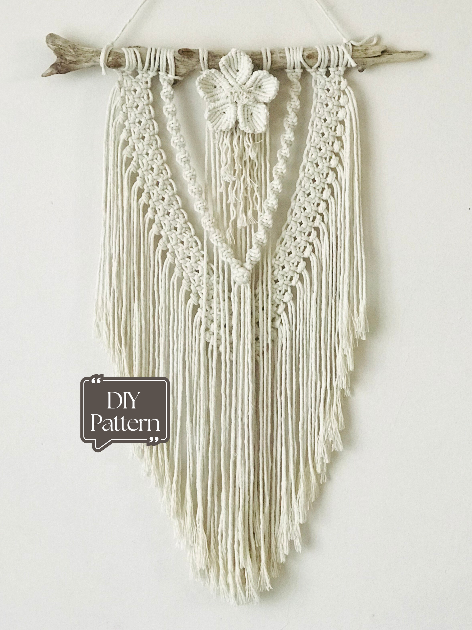 Macrame wall hanging on a white wall with a plant in the foreground
