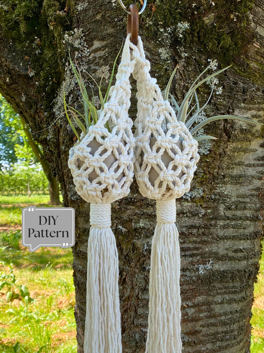 Double macramé plant hanger with two small pots attached to a single wooden ring, featuring decorative knotting and tassels, hanging outdoors on a tree; DIY macramé PDF pattern.