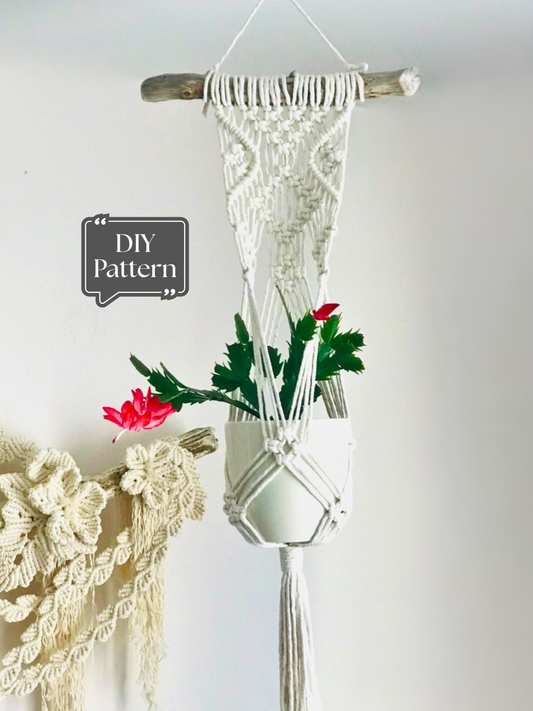 White macramé wall-mounted plant hanger with a decorative knotted design, hanging from a wooden branch and holding a potted plant indoors; DIY macramé PDF pattern