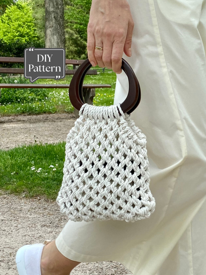 Handmade mini macramé bag with wooden handles, shown being carried by hand outdoors, featuring an open knot pattern and natural cotton cord.