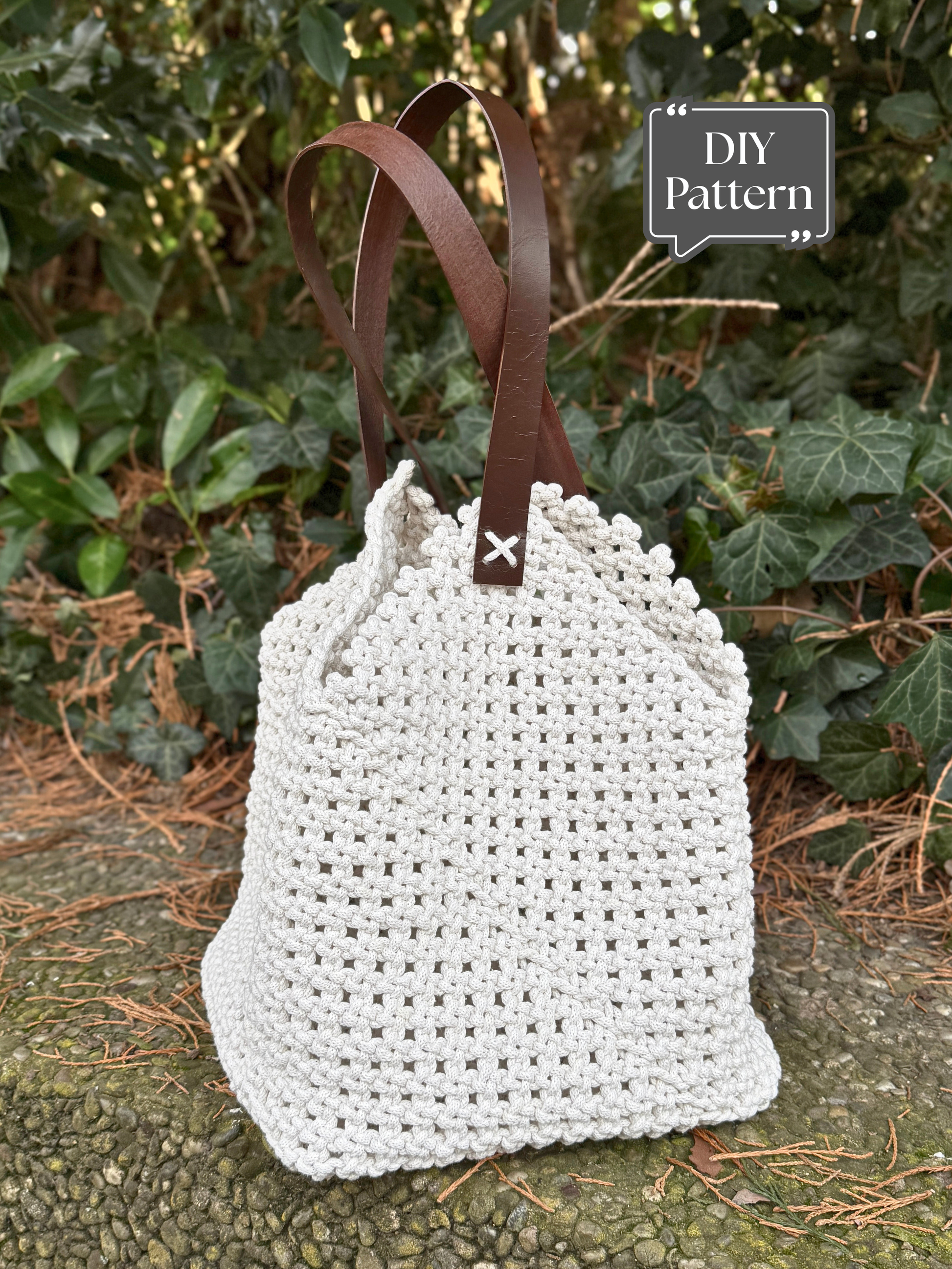 DIY macramé bag pattern with leather handles, featuring a textured knotted design and a soft drawstring-style top, photographed outdoors against green foliage.