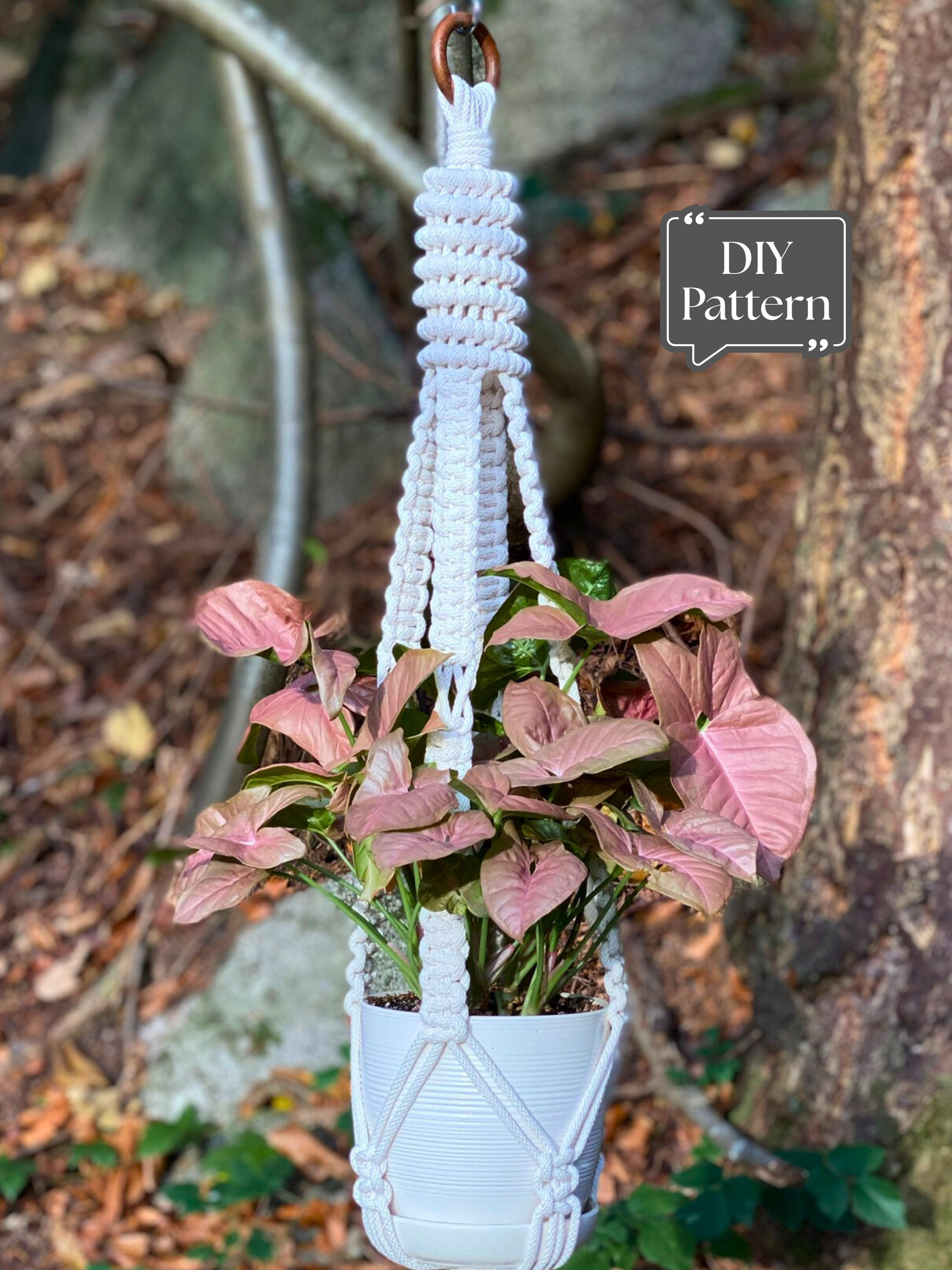 Macrame plant hanger with spiral knot design holding white pot and pink green plant outdoors, DIY pattern example